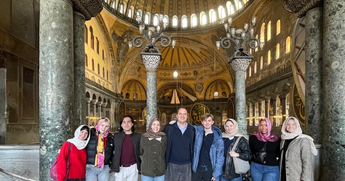 Student group with the Hagia Sophia main gallery's frescoed ceiling behind them.