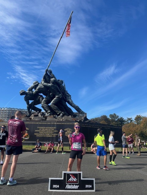 Dara Ford poses with Marine Corps Ultramarathon finisher sign in front of Marine Corps War Memorial