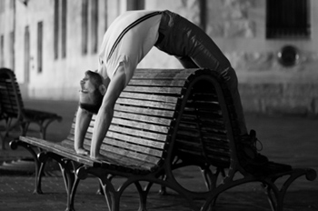 A Street Light Circus bending backward over a bench