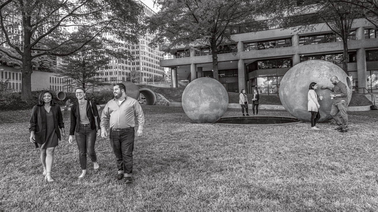 Seven AU alumni stand near a fountain in Dark Star Park in Rosslyn