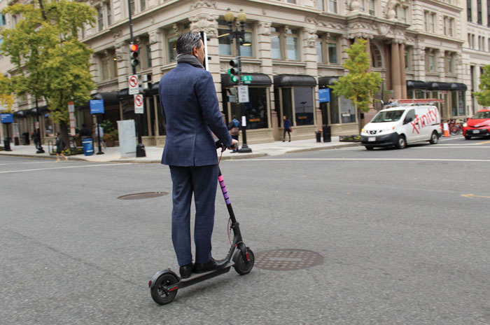 man in a suit rides a scooter through the streets of DC