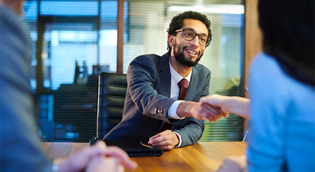 Man and woman seated at table shaking hands during meeting