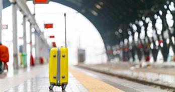 A bright yellow suitcase stands on an empty platform. travel background. blurred background