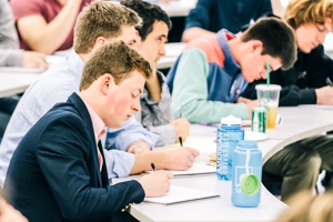 A student takes notes while sitting in a lecture hall.