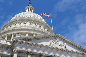 The dome of the US Capitol Building with the US flag flying and blue sky