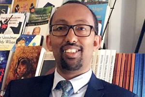 Man smiling with glasses in front of books.