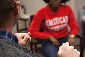 Photo of two people, one white and one black, their faces obscured, speak to each other.